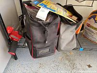 Photo of two tool bags, one black with red trim and another gray with orange accents, containing miscellaneous tools and packages