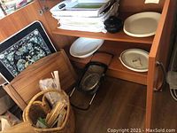 Shelf with stacked ceramic and plastic platters and trays, white and beige in color, a black metal stand and wooden cutting boards.