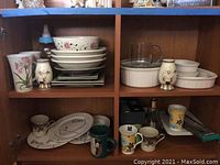 Wide view of kitchen cabinet shelf with Corning Ware bowls and casseroles, mugs, tea cups, and salt and pepper shakers