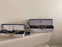 Two Bradford Exchange charm bracelets and a small black jewelry box containing ring, displayed on a shelf