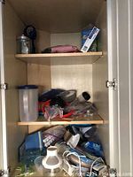 Wide view inside one kitchen cabinet showing assorted kitchen items including storage containers, kitchen tools, and cookware on two wooden shelves.