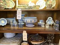 Full shelf showing all Wedgwood blue jasperware items, silver plated spoon, and other decorative objects placed on wooden shelf.