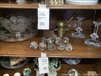 Shelf display showing frosted glass bowl and plate, brass mortar and pestle, eight crystal eggs in front, and two clear crystal candle holders.