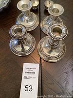 Four sterling candlestick holders and two small lidded salt servers arranged on dark table surface