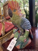 Front and side view of the wood carved bird statue showcasing colors and detailed feathers on a green carved base.