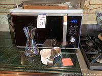 Samsung microwave on kitchen counter with carafe and trays in front.