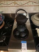 Photo of four Japanese iron tea pots arranged on a stovetop: one large standard teapot and three miniature teapots on a tray.