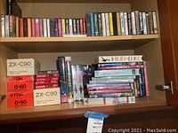 Upper cabinet shelf showing blank audio cassette boxes and a selection of VHS and DVD titles
