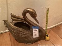 Side view of metal swan planter beside measuring tape showing height around 12 inches