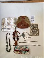Overview photo showing two purses, multiple necklaces including bead necklaces and a dragon-embossed metal jewelry piece, plus a floral fabric zippered pouch.