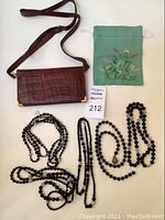 Full lot layout showing the brown animal skin bag with adjustable strap in croc pattern, three different vintage black bead necklaces arranged flat, and a small green embroidered drawstring pouch.