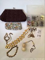 Full lot overview showing two handbags (brown knit clutch and beaded multi-colored square handbag), various gold-tone jewelry pieces including carved elephant necklace, and a container with buttons.
