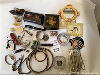 Full lot arranged on flat surface showing carved cat mirror, black lacquered boxes with floral paint, red Swiss Army knife, magnifying glass, pill box, watches, letter openers, headbands, and other small items.
