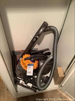 Photo of a Dyson vacuum with hose, multiple accessory attachments, and a box in a storage space.