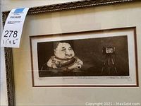 Framed sepia-toned art print signed and numbered, showing a caricature figure and a vintage camera.