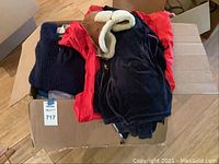 Large box filled with folded men's dress shirts and other clothing items, including a black and red velour track suit top visible on top.