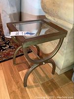 Side angle view of the metal and glass small table showing the curved legs and glass top.