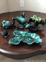 Collection of six pottery items on a brown table, including animal figurines and a leaf-shaped dish in blue and green colors.