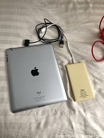 Silver Apple iPad back with Apple logo and connected USB cable to yellow power bank.