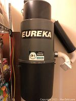 Front view of Eureka brand central vacuum unit installed on wall showing model CV-1 with piping attached.