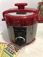 Front view of Wolfgang Puck multi cooker in red and stainless steel, showing control knob and handle on lid.