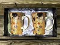 Two fine bone china mugs featuring Gustav Klimt's The Kiss artwork, packaged in a satin-lined gift box.