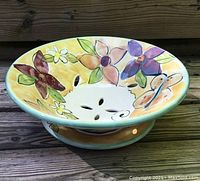 Side angled photo showing the colorful floral hand painted design and cut-out drainage holes of the pottery berry bowl.