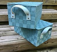 Two blue woven flip-top storage baskets stacked on outdoor steps showing the front and side handles.