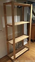 Wooden shelf unit shown fully assembled with three shelves in place and vertical supports with drilled holes visible.