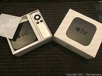Apple TV device and remote inside original white box with lid partly off, placed on a dark surface.