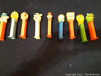 Nine PEZ dispensers lying down showing character heads and colored stems.
