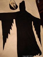 Full view of black hooded robe laid flat showing jagged, pointed sleeve ends and hood.