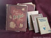 Five antique books displayed on a red surface, showing covers with visible wear and age, including Hill's Manual of Business Forms with distinctive red cover and decorative elements.