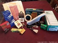 Photo showing various office supplies arranged on a table including a heavy duty stapler, staple remover, index dividers, Post-it Notes, Scotch tape, labels, and binder clips.