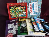 Puzzle books arranged showing various titles including 'Amazing Mazes', 'Where's Waldo?', jumbo Sudoku, Kakuro, and several smaller Sudoku and Kakuro booklets in plastic sleeves.