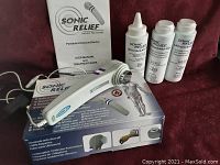 Photo showing the Sonic Relief portable ultrasound device with user manual, treatment book, power adapter, and two bottles of ultrasound gel.