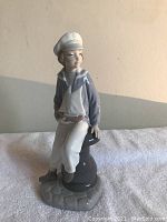 Front angle of the Lladro sailor boy figurine showing the front of the figure with sailor hat, jacket, and base resembling sailboat cleat and deck.