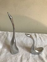 Two metal swan sculptures shown side by side on a white cloth background
