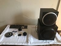 Photo showing two black Logitech speakers with silver circular covers, a wired keyboard, and multiple small round electronics on a white towel