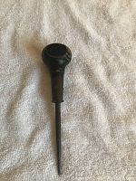 Single antique awl laid on a light-colored textured fabric background, showing entire wooden handle and metal pointed shaft in clear detail.