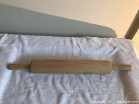 Wooden rolling pin placed on white towel showing full length and handles.