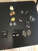 Photo showing 12 assorted earrings on a black surface, including teardrop, leaf dangle, and multiple stud styles on display cards or loose.