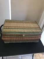 Closed woven sewing basket with handle and lid showing woven pattern and a small closure button.