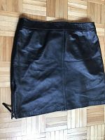 Full view of black leather mini skirt laid flat showing front side and zipper detail at bottom left.