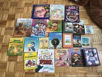 Photo showing collection of 22 assorted children's books and 2 DVDs arranged on floor, including titles with animals, holiday themes, counting, and classic stories.