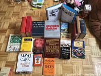 Top-down photo showing 17 assorted books including dictionaries, novels, health guides, cooking, and art related books arranged on a parquet wooden floor.