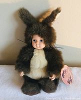 Front view of baby squirrel plush doll with furry brown and cream squirrel costume, realistic baby face, and bushy tail.