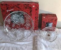 Photo of two German glassware items in front of their original red rose patterned boxes. Left is a large round platter divided into sections with embossed roses, right is a smaller round bowl with handle and similar rose design.