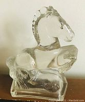 Front and side view of the heavy glass horse figurine showing prancing stance, detailed mane, tail, and solid clear glass construction.