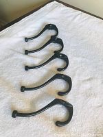Four heavy, sturdy black metal coat hooks laid out in a row on a white towel, showing their strong curved design and mounting holes.